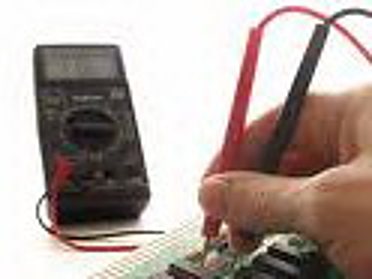 Une main place la sonde rouge d'un multimètre numérique sur un circuit monté sur une plaque d'essai pour effectuer une mesure.