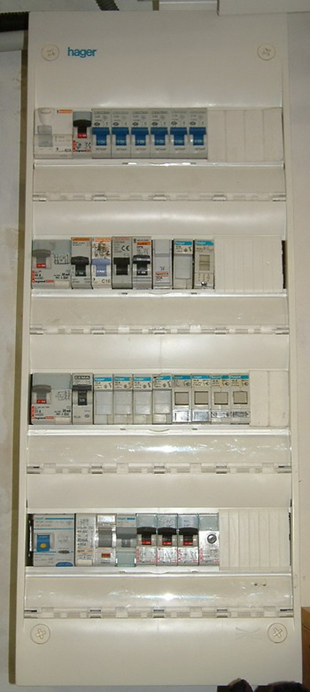 Tableau électrique blanc de marque Hager ouvert, montrant quatre rangées de disjoncteurs et d'interrupteurs différentiels fixés sur des rails.